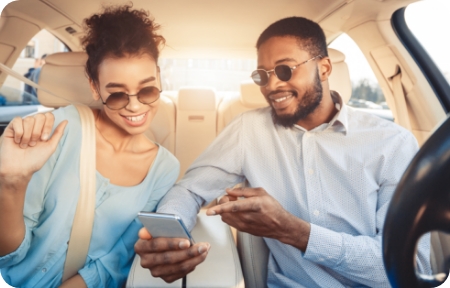 Young couple sit in a parked vehicle and look at cellphone together.